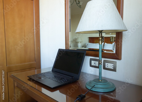 Laptop on a small table next to a lamp and a mirror.