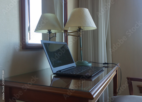 Laptop on a small table next to a lamp and a mirror.