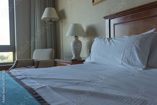 Hotel room with lamps , a chair and pillows on the bed.