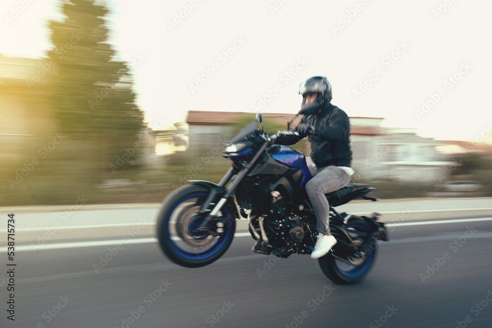 Side view of a motorcycle rider riding race motorcycle on a wheelie the highway with motion blur.