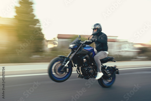 Side view of a motorcycle rider riding race motorcycle on a wheelie the highway with motion blur. photo