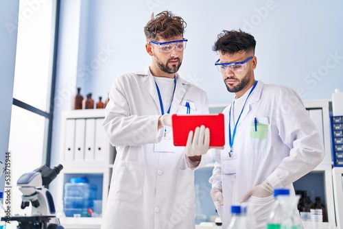 Young couple wearing scientist uniform using touchpad at laboratory