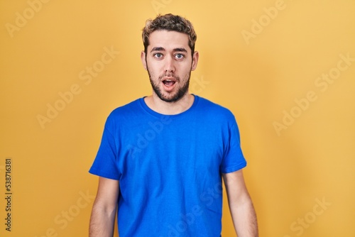 Hispanic man with beard standing over yellow background afraid and shocked with surprise and amazed expression, fear and excited face.