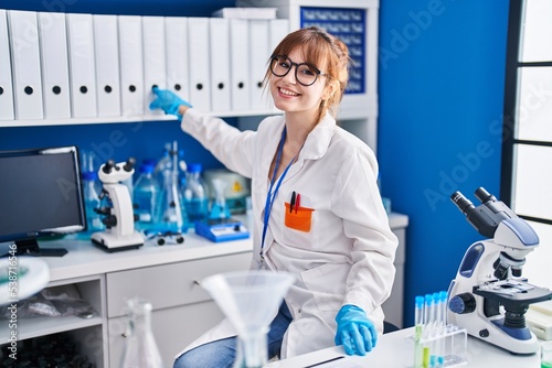 Young woman scientist smiling confident holding binder at laboratory