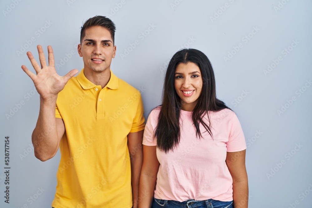 Young couple standing over isolated background showing and pointing up with fingers number five while smiling confident and happy. Young couple standing over isolated background showing and pointing up with fingers number five while smiling confident and happy.