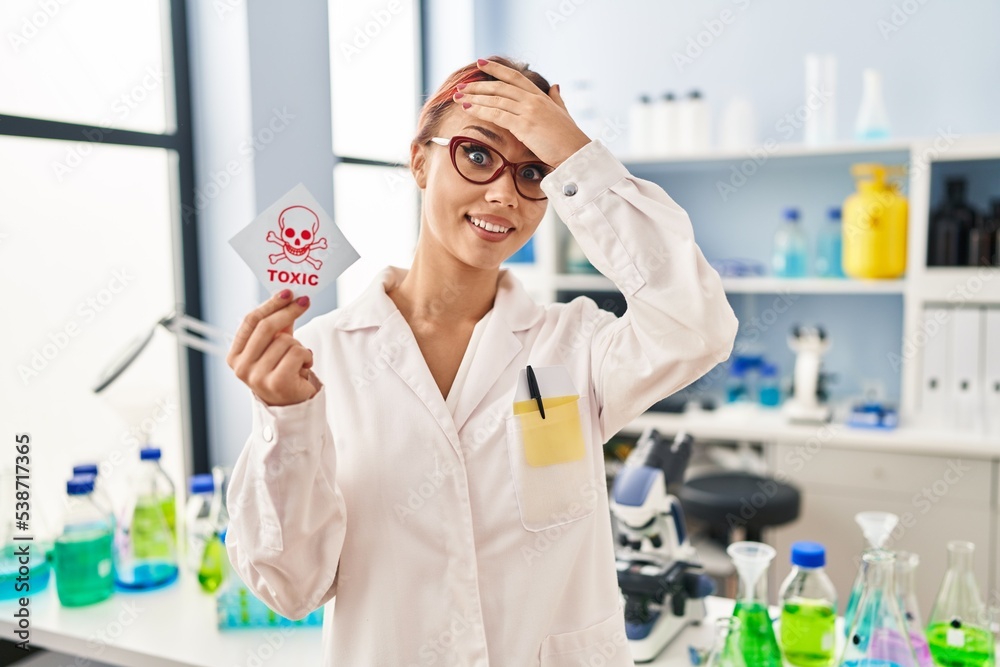 Young caucasian woman working at scientist laboratory holding toxic label stressed and frustrated with hand on head, surprised and angry face Young caucasian woman working at scientist laboratory holding toxic label stressed and frustrated with hand on head, surprised and angry face