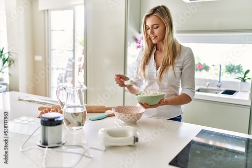 Young blonde woman smiling confident pouring flour on bowl at kitchen