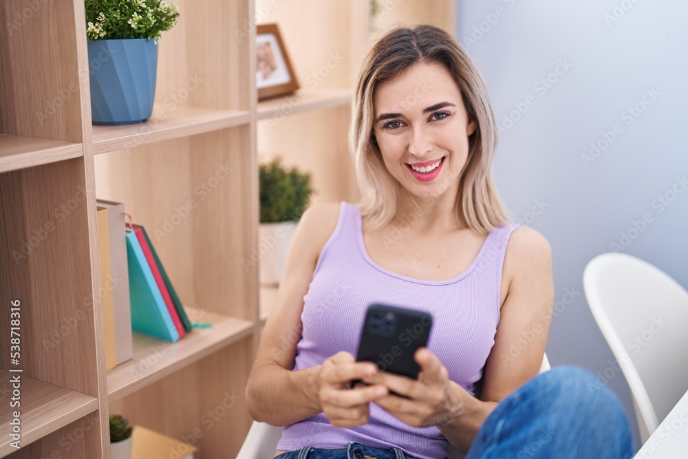 Young woman using smartphone sitting on chair at home Young woman using smartphone sitting on chair at home