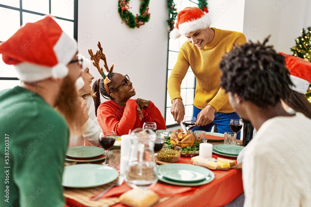 Group of young people smiling happy having christmas dinner, Man cutting roasted turkey to serve at home. Group of young people smiling happy having christmas dinner, Man cutting roasted turkey to serve at home.