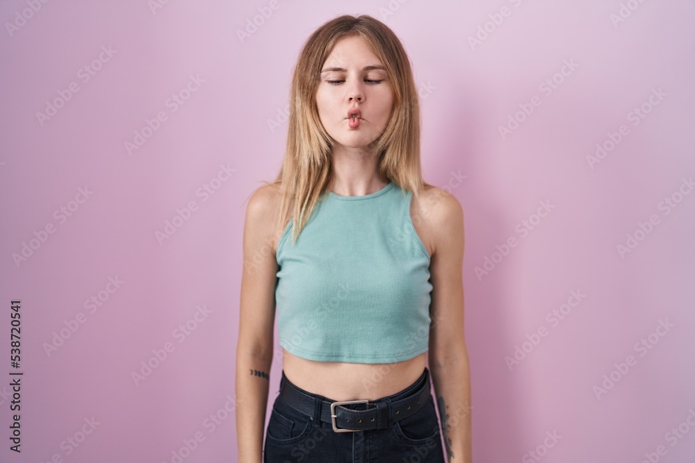 Blonde caucasian woman standing over pink background making fish face with lips, crazy and comical gesture. funny expression. Blonde caucasian woman standing over pink background making fish face with lips, crazy and comical gesture. funny expression.