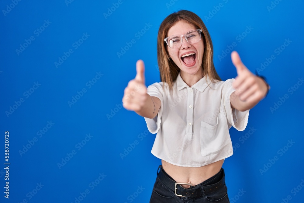 Beautiful woman standing over blue background approving doing positive gesture with hand, thumbs up smiling and happy for success. winner gesture. Beautiful woman standing over blue background approving doing positive gesture with hand, thumbs up smiling and happy for success. winner gesture.