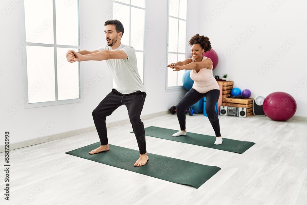 Young african american woman and hispanic man exercising at pilates room, stretching body and doing yoga pose, training strength and balance Young african american woman and hispanic man exercising at pilates room, stretching body and doing yoga pose, training strength and balance