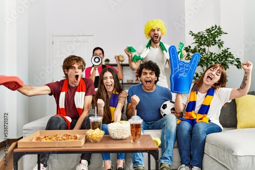 Group of young hispanic friends watching and supporting soccer match at home.