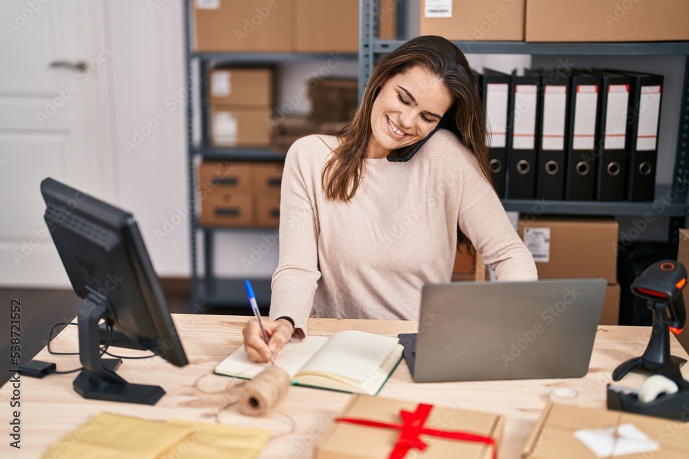 Young beautiful hispanic woman ecommerce business worker talking on smartphone writing on notebook at office Young beautiful hispanic woman ecommerce business worker talking on smartphone writing on notebook at office