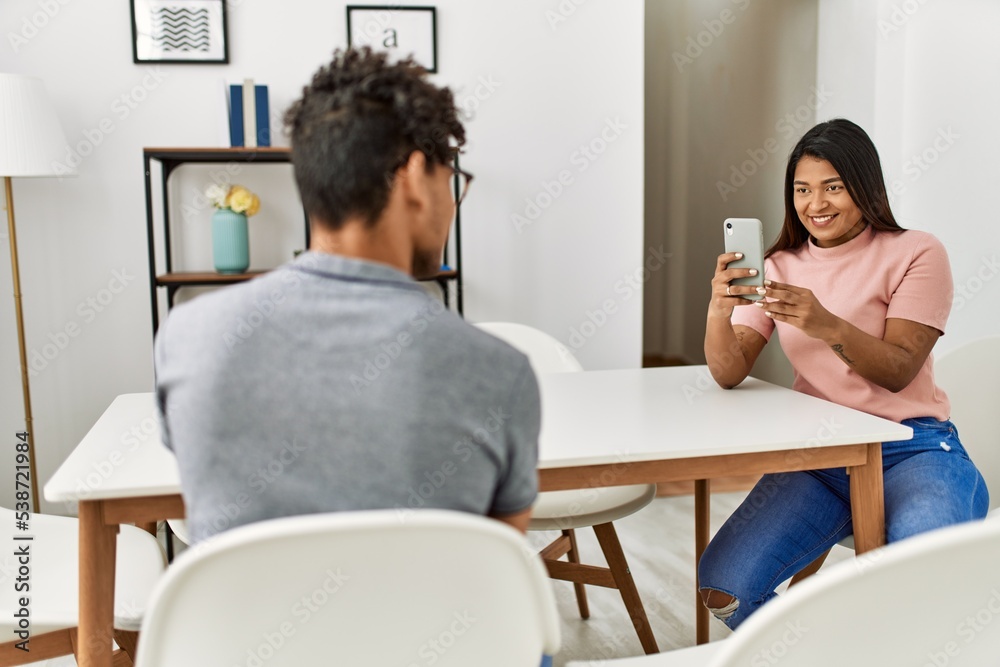 Young latin woman making man picture using smartphone at home.