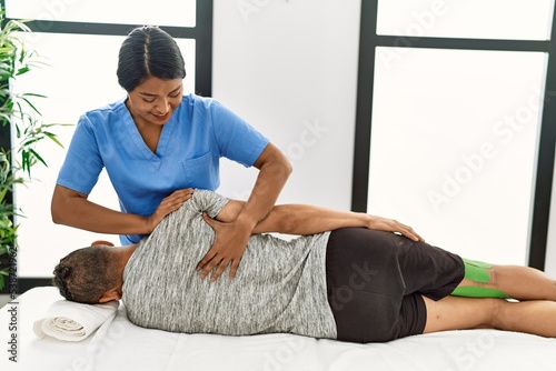 Young latin physioterapist woman make back rehab treatment to hispanic man at the clinic. photo