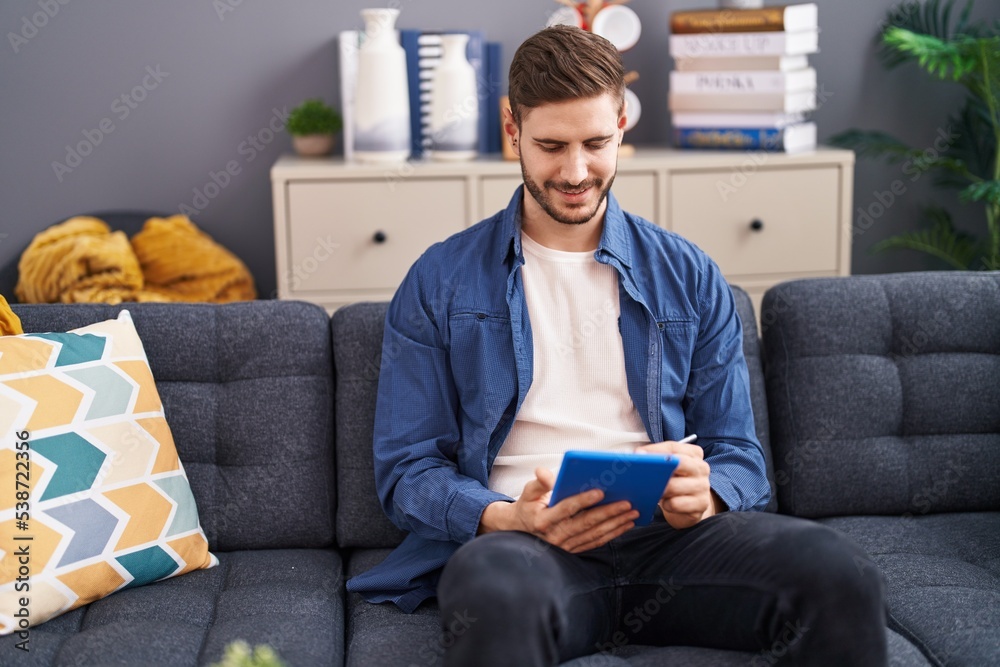 Obraz premium Young caucasian man using touchpad sitting on sofa at home