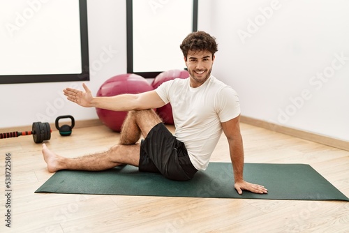 Young hispanic man smiling confident stretching at sport center