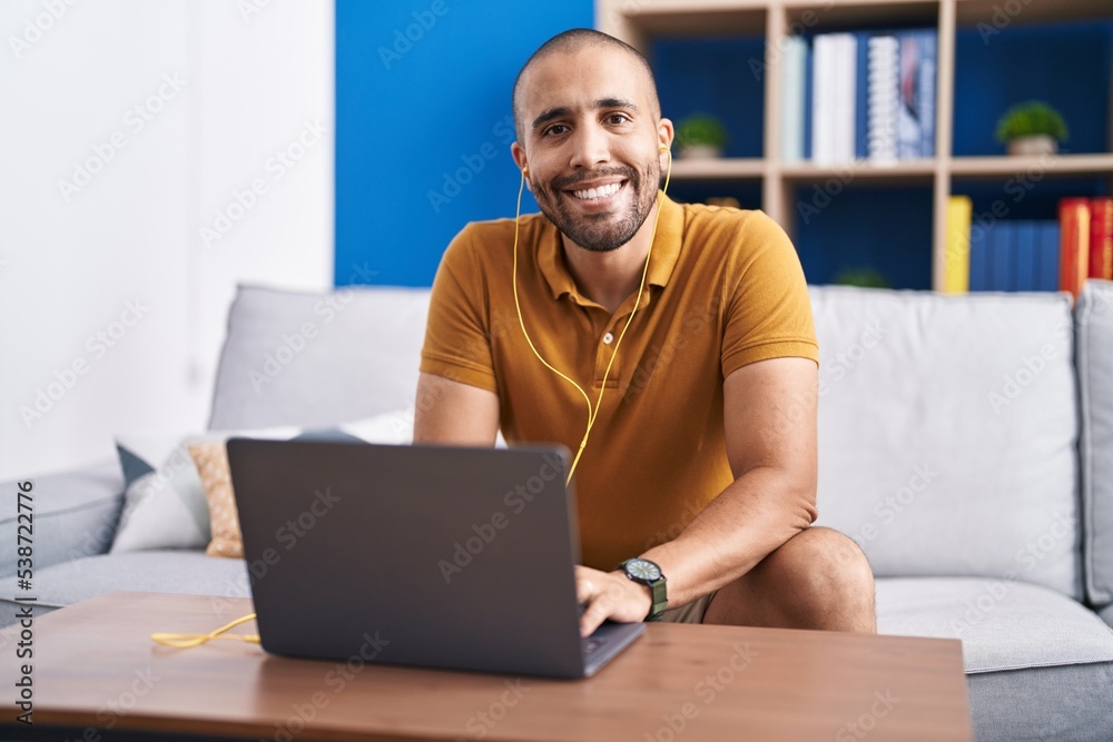 Young latin man using laptop and headphones sitting on sofa at home Young latin man using laptop and headphones sitting on sofa at home