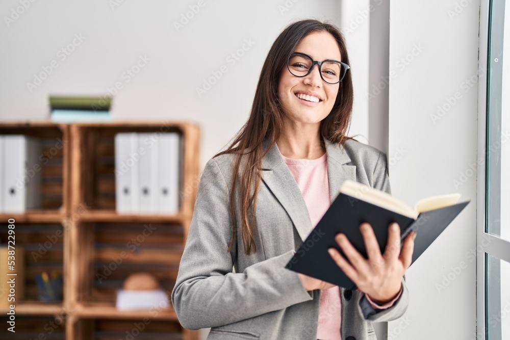 Young woman psychologist smiling confident reading book at psychology center Young woman psychologist smiling confident reading book at psychology center