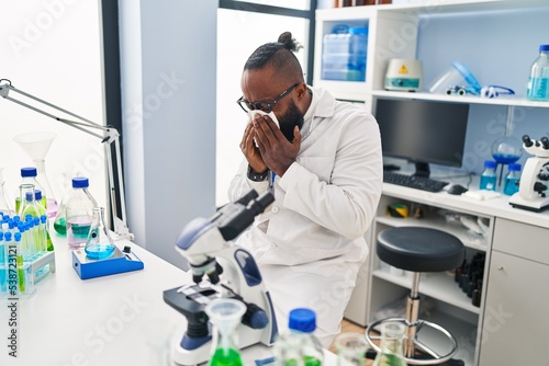 Young african american man wearing scientist uniform illness using napkin at laboratory
