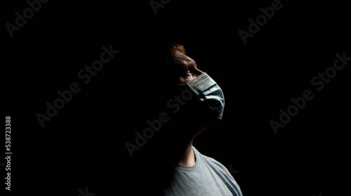 Male wearing surgical mask on a dark background.