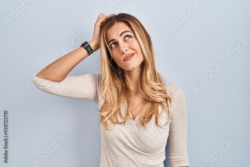 Young blonde woman standing over isolated background confuse and wondering about question. uncertain with doubt, thinking with hand on head. pensive concept.