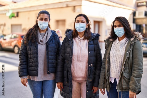 Three woman mother and daughters wearing medical mask standing together at street
