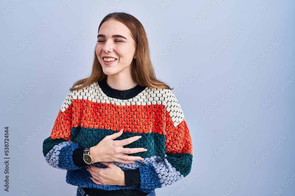 Young hispanic girl standing over blue background smiling and laughing hard out loud because funny crazy joke with hands on body.