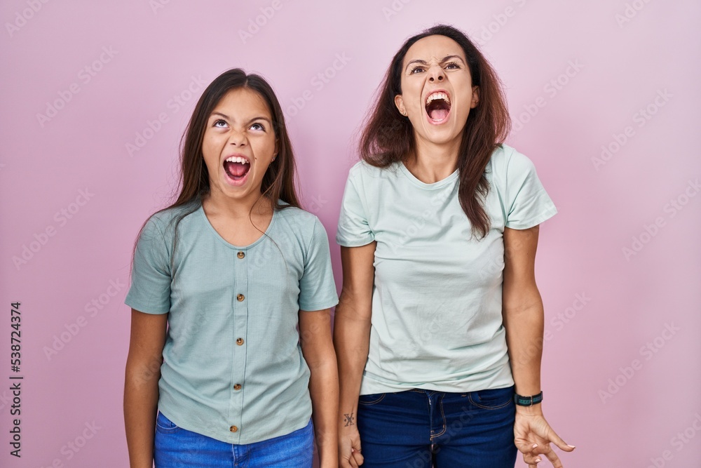 Young mother and daughter standing over pink background angry and mad screaming frustrated and furious, shouting with anger. rage and aggressive concept. Young mother and daughter standing over pink background angry and mad screaming frustrated and furious, shouting with anger. rage and aggressive concept.