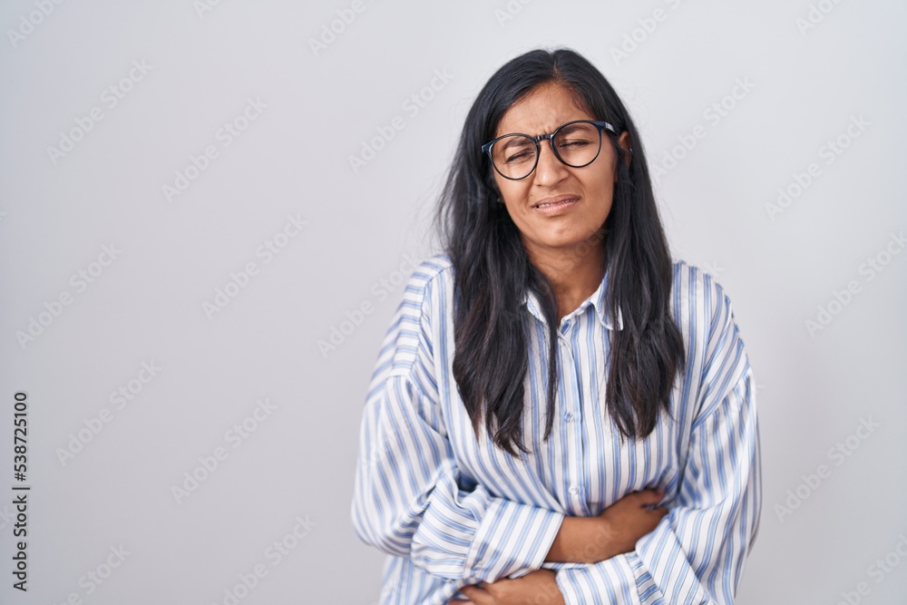 Young hispanic woman wearing glasses with hand on stomach because indigestion, painful illness feeling unwell. ache concept. Young hispanic woman wearing glasses with hand on stomach because indigestion, painful illness feeling unwell. ache concept.