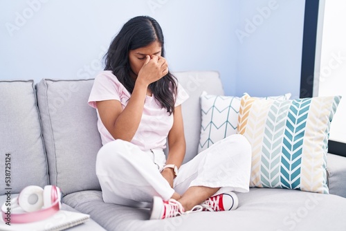 Young hispanic woman sitting on the sofa at home tired rubbing nose and eyes feeling fatigue and headache. stress and frustration concept.