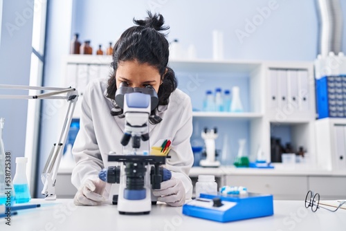 Young latin woman scientist smiling confident using microscope at laboratory