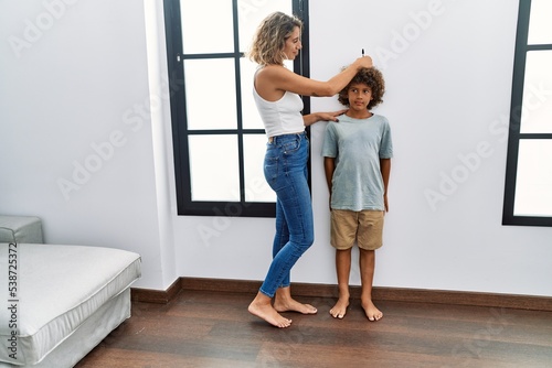 Mother and son measuring child height drawing mark on wall at home