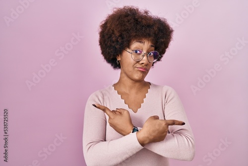 Young african american woman standing over pink background pointing to both sides with fingers, different direction disagree