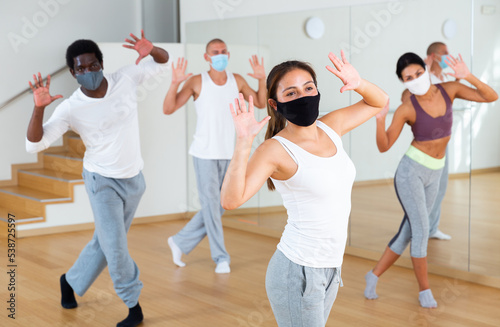 Portrait of young hispanic woman wearing protective mask enjoying active dancing during group training in dance studio. Precautions in coronavirus pandemic