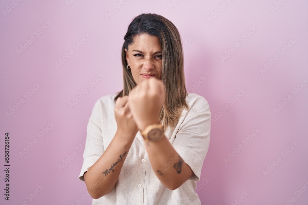 Blonde woman standing over pink background ready to fight with fist defense gesture, angry and upset face, afraid of problem Blonde woman standing over pink background ready to fight with fist defense gesture, angry and upset face, afraid of problem