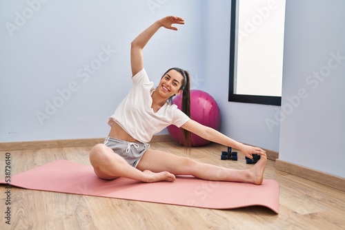 Young beautiful hispanic woman smiling confident stretching leg at sport center