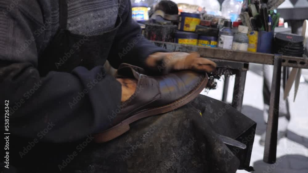 Shoemaker rubs shoes with cream on the street repairing shop, close up. Shoe manufacturing workshop, craftsman cleans and polishes leather boots. Shoemaker rubs shoes with cream on the street repairing shop, close up. Shoe manufacturing workshop, craftsman cleans and polishes leather boots.