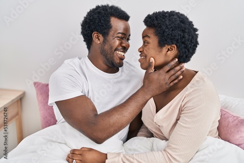 African american man and woman couple hugging each other sitting on bed at bedroom