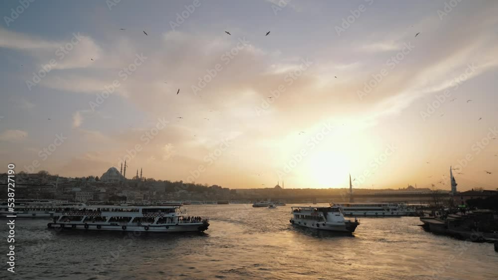 View from Galata Bridge: Ferry boats passing by Bosphorus at sunset, seagulls flying above, Golden Horn bridge. Sea transport traffic, vessels and ships sailing, Istanbul, Turkey View from Galata Bridge: Ferry boats passing by Bosphorus at sunset, seagulls flying above, Golden Horn bridge. Sea transport traffic, vessels and ships sailing, Istanbul, Turkey