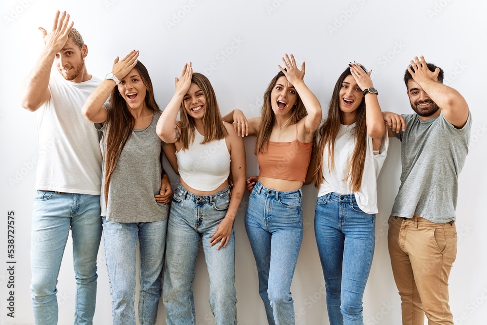 Group of young friends standing together over isolated background surprised with hand on head for mistake, remember error. forgot, bad memory concept.