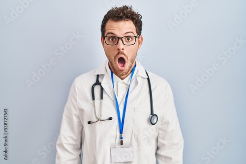 Young hispanic man wearing doctor uniform and stethoscope afraid and shocked with surprise expression, fear and excited face.