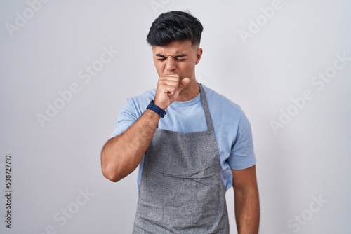 Hispanic young man wearing apron over white background feeling unwell and coughing as symptom for cold or bronchitis. health care concept.