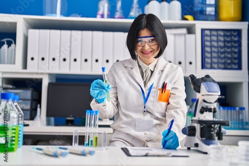 Young chinese woman scientist holding test tube write on report document at laboratory