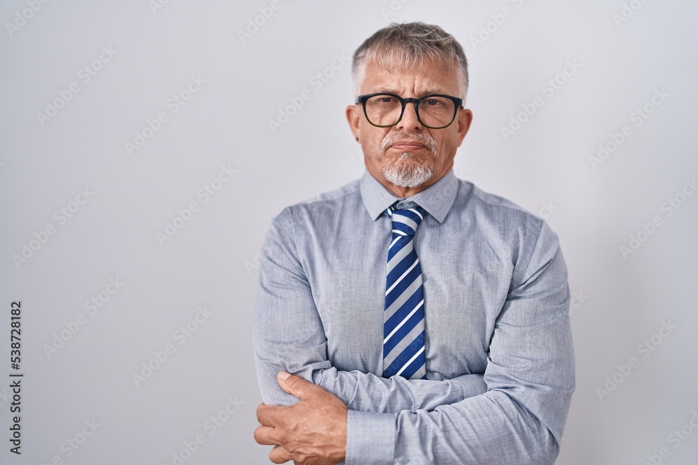 Hispanic business man with grey hair wearing glasses skeptic and nervous, disapproving expression on face with crossed arms. negative person. Hispanic business man with grey hair wearing glasses skeptic and nervous, disapproving expression on face with crossed arms. negative person.