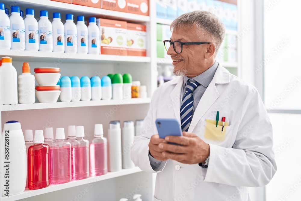 Middle age grey-haired man pharmacist using smartphone working at laboratory