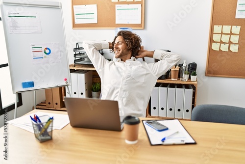 Young hispanic businessman relaxed with hands on head sitting on the table at office.