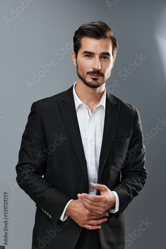 A man in a business suit businessman poses against a gray background straightening his tie and looking at the camera © SHOTPRIME STUDIO