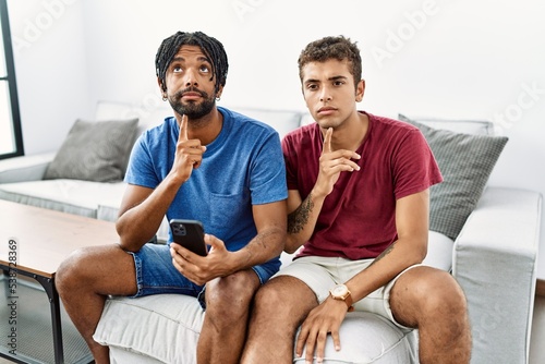 Fotografie Young hispanic men using smartphone sitting on the sofa at home thinking concent